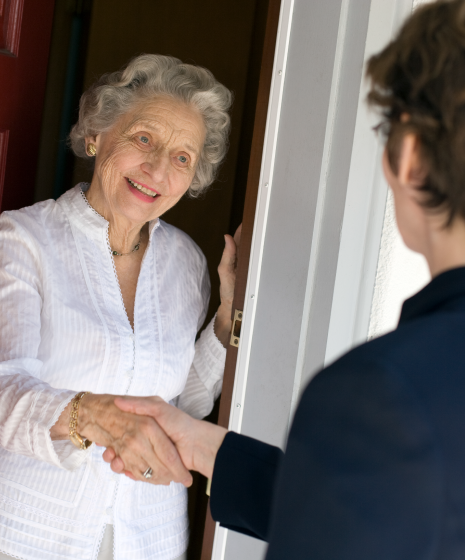 senior woman opening door and shaking hands with young person